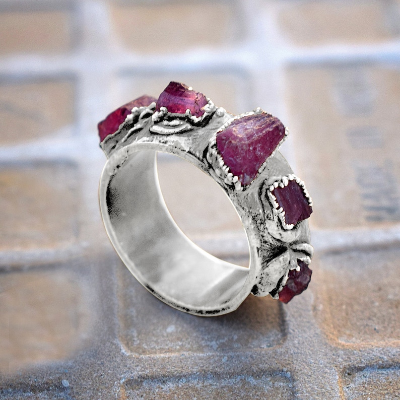 Pode incluir: Um anel de prata com uma banda decorada com um design floral e cravejada com cinco pedras preciosas cor-de-rosa.