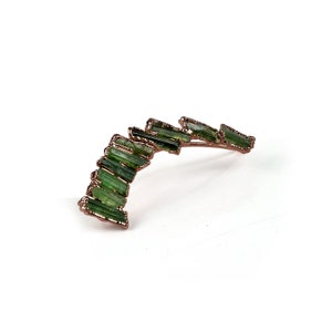 Puede incluir: Un pendiente de turmalina verde con un dise&ntilde;o curvo. El pendiente est&aacute; hecho de alambre de cobre y presenta una fila de piedras de turmalina verde.