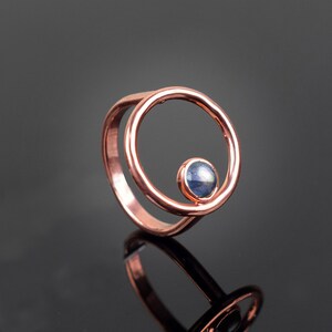 Puede incluir: Un anillo de cobre con una sola piedra preciosa azul engastada en un dise&ntilde;o circular.