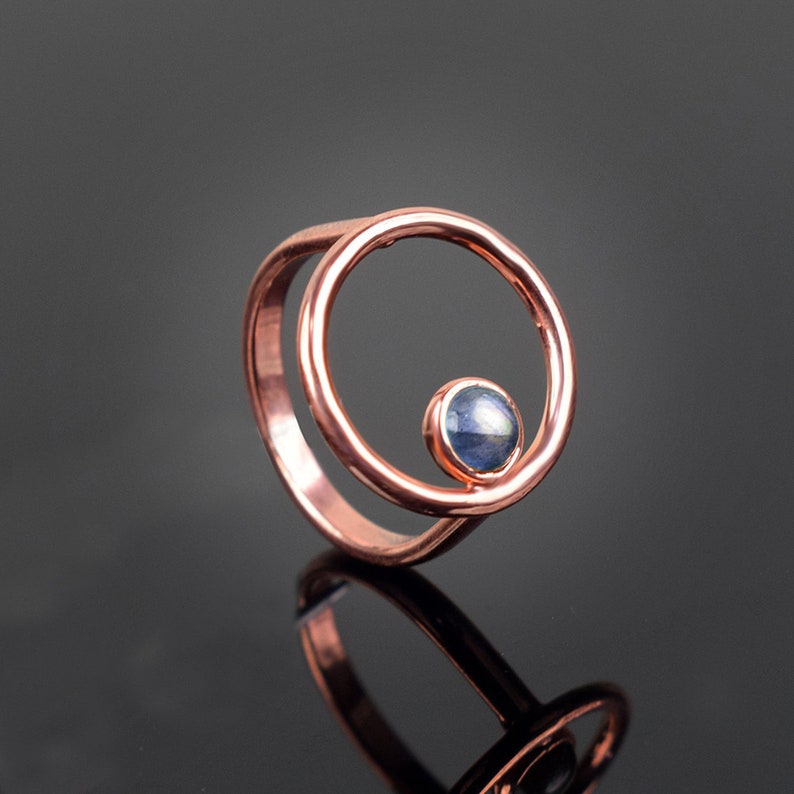 Puede incluir: Un anillo de cobre con una sola piedra preciosa azul engastada en un dise&ntilde;o circular.