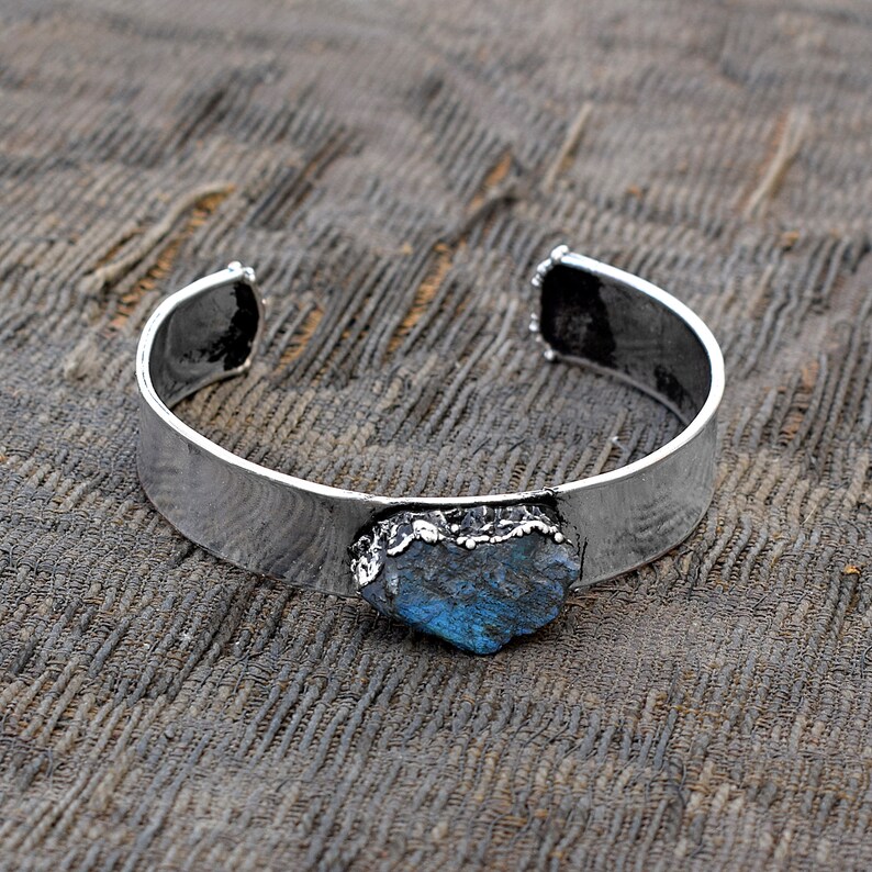May include: A silver cuff bracelet featuring a large, blue-green gemstone set in the centre. The gemstone has a rough, natural appearance.