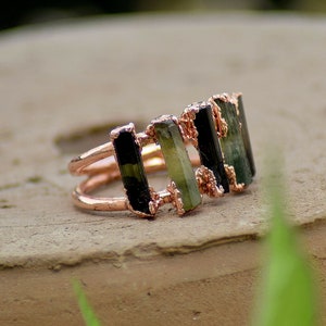May include: A rose gold ring with five green and black gemstone bars set in a double band.