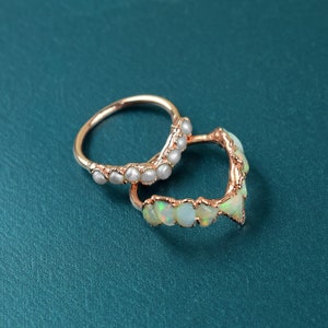 Op de afbeelding: Twee gouden ringen met witte edelstenen. De ene ring heeft een rij kleine, ronde witte edelstenen, terwijl de andere een rij grotere, onregelmatig gevormde witte edelstenen heeft.
