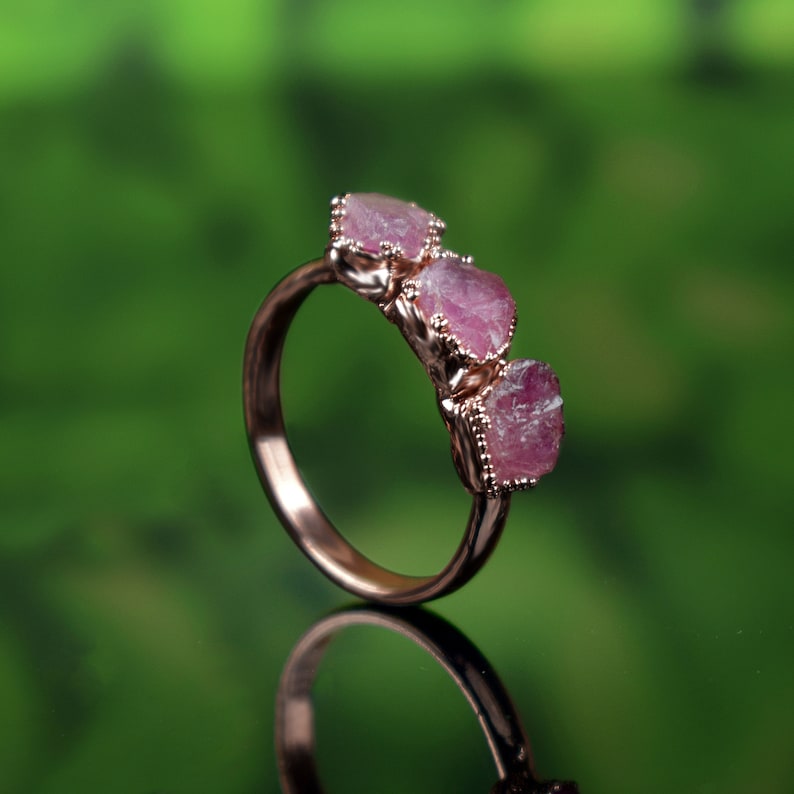 May include: A rose gold ring with three pink, raw, gemstone accents.