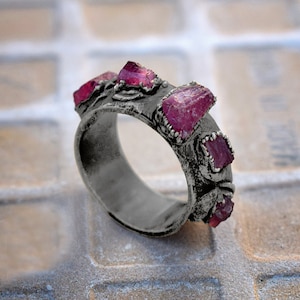 Pode incluir: Um anel de prata com uma banda texturizada e cinco pedras preciosas cor-de-rosa engastadas na banda.