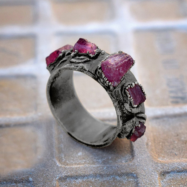 Pode incluir: Um anel de prata com uma banda texturizada e cinco pedras preciosas cor-de-rosa engastadas na banda.