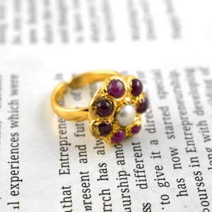 May include: A gold ring with a flower design featuring a pearl in the center and pink gemstones around it.