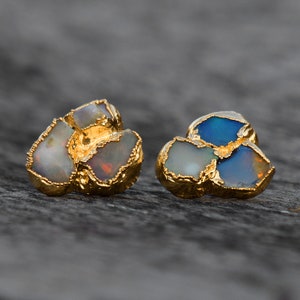 May include: A pair of gold earrings with opal stones. The earrings are made of three pieces of opal each, with one piece being a darker blue color and the other two being a lighter white color.