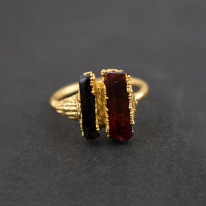 May include: Gold ring with two rectangular gemstones, one black and one red, set in a textured gold band.