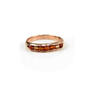 May include: A rose gold band ring with a row of carnelian gemstones.