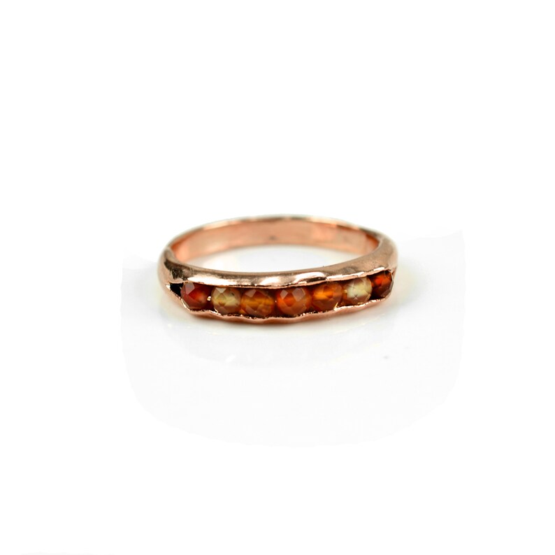 May include: A rose gold band ring with a row of carnelian gemstones.