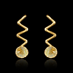 May include: A pair of gold earrings with a zig-zag design and a round, clear stone with gold flecks.