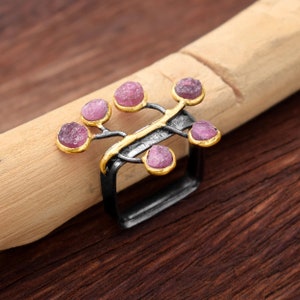 May include: A silver ring with a gold accent and pink gemstones set in a branch-like design.