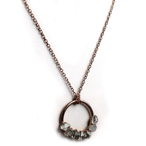 Puede incluir: Un collar de oro rosa con un colgante circular que presenta un grupo de piedras preciosas sin pulir de color gris claro.