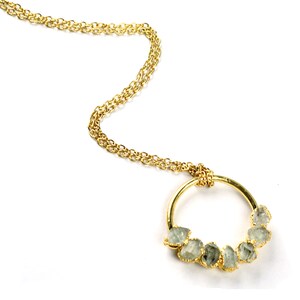 Puede incluir: Un collar de cadena dorada con un colgante circular que presenta un grupo de piedras preciosas de color verde claro.