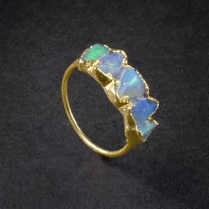 Op de afbeelding: Een gouden ring met een band van ruwe, iriserende opaalstenen. De stenen zijn gezet in een gouden band en tonen een mix van blauw, groen en wit.