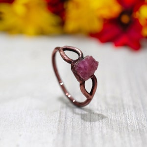 May include: A copper ring with a delicate, leaf-shaped design and a pink gemstone set in the center.