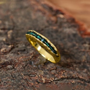 May include: A gold band ring with a row of emerald green gemstones set into the band.