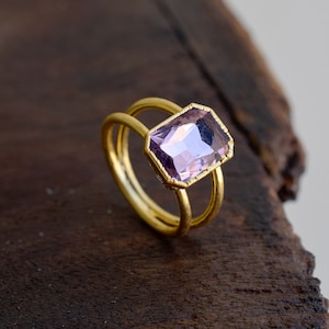 May include: A gold ring with a double band design features a large, rectangular, faceted amethyst gemstone.