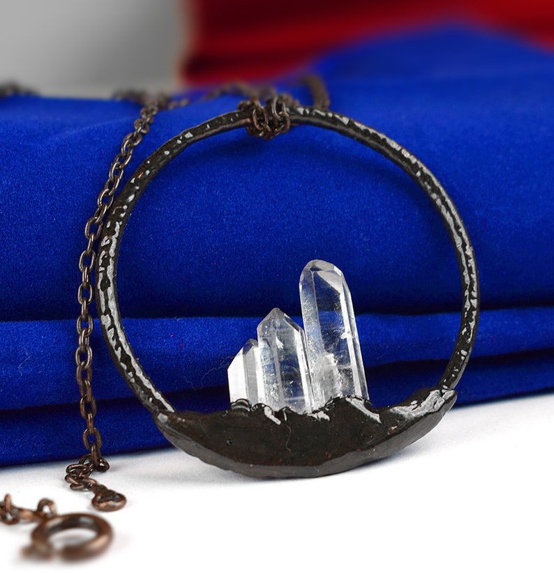 Op de afbeelding: Een zilveren ketting met een zwarte metalen cirkel hanger met drie heldere kwartskristallen. De hanger is gevormd als een bergketen.