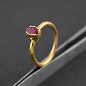 May include: A gold ring with a deep red oval gemstone. The ring has a textured band.