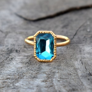 May include: A gold ring with a large, blue, rectangular-shaped gemstone.