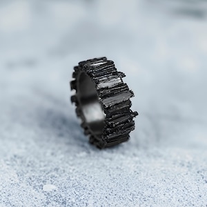 Könnte beinhalten: Ein schwarzer Ring mit einem strukturierten, gezackten Design. Der Ring ist aus Metall und hat eine matte Oberfläche.