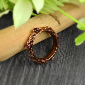 May include: A copper ring with a textured design and small pink gemstones set into the band.