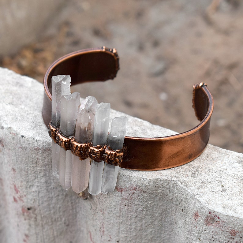May include: A copper bracelet with clear quartz crystals attached. The crystals are arranged in a vertical row and are held in place by copper wire.