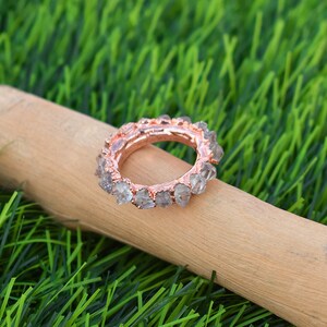 Puede incluir: Un anillo de oro rosa con una banda de cristales transparentes y facetados. El anillo est&aacute; sobre una superficie de madera.