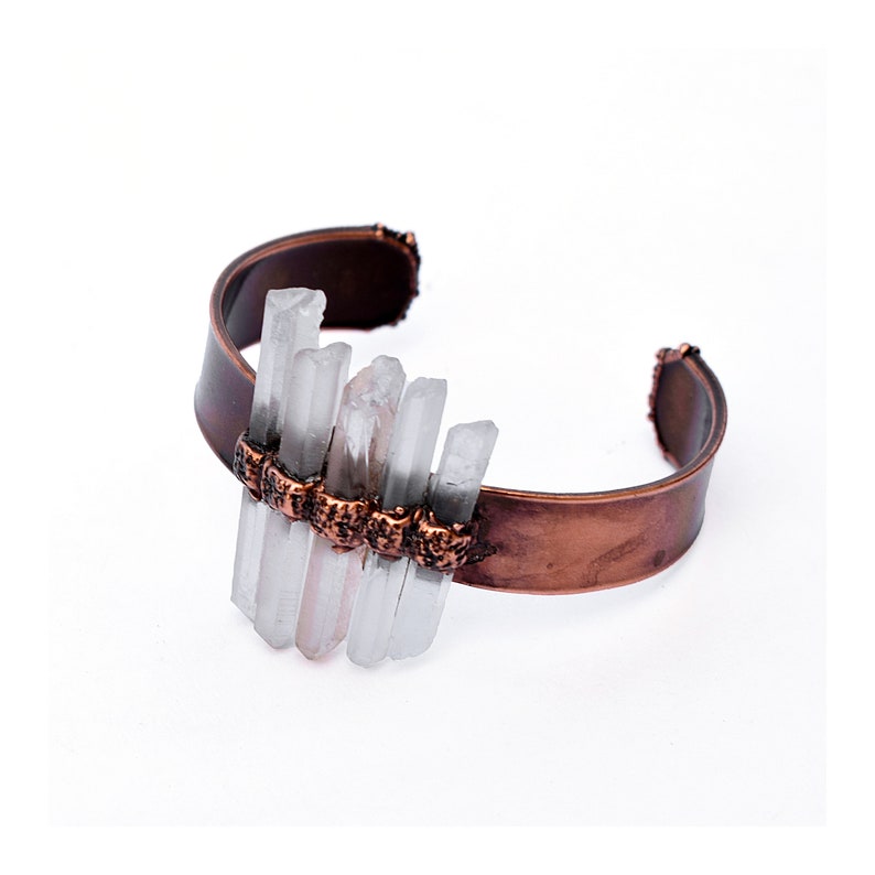 May include: A copper cuff bracelet with a cluster of clear quartz crystals attached to the front. The crystals are arranged in a staggered pattern and are held in place by small copper beads.