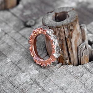 Puede incluir: Un anillo de oro rosa con una banda de peque&ntilde;as piedras facetadas transparentes. El anillo est&aacute; sobre un trozo de madera desgastada.
