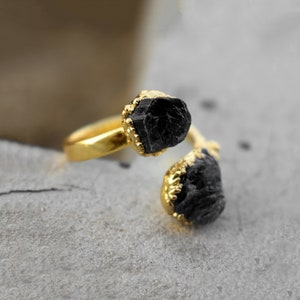 Peut inclure: Une bague en or avec deux pierres noires brutes. Les pierres sont serties dans des chatons en or et la bague est ouverte.