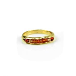 May include: A gold band ring with a row of orange gemstones.