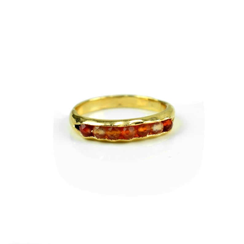 May include: A gold band ring with a row of orange gemstones.