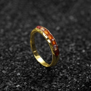 May include: A gold band ring with a row of orange and red gemstones.