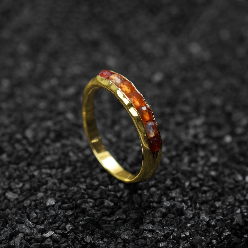May include: A gold band ring with a row of orange and red gemstones.