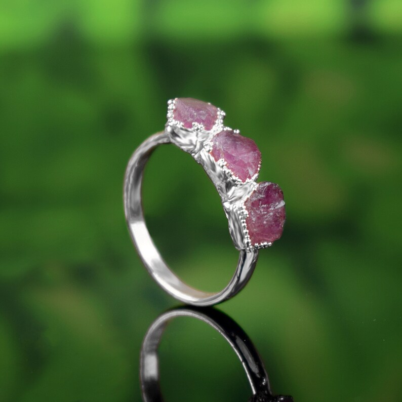 May include: A silver ring with three pink ruby stones set in the band.