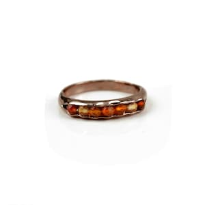 May include: A rose gold band ring with a row of orange carnelian gemstones.