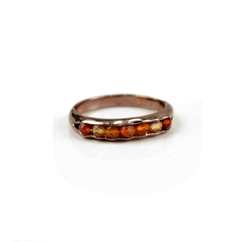May include: A rose gold band ring with a row of orange carnelian gemstones.