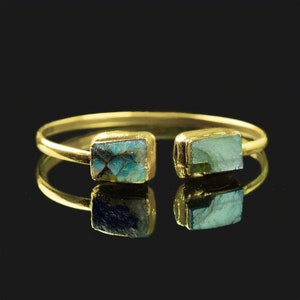 May include: A gold bangle bracelet with two square-shaped blue and green gemstone accents.
