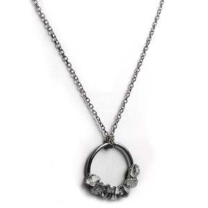 Puede incluir: Un collar de cadena de plata con un colgante circular de plata que presenta un grupo de piedras transparentes y facetadas.