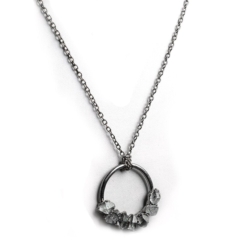 Puede incluir: Un collar de cadena de plata con un colgante circular de plata que presenta un grupo de piedras transparentes y facetadas.