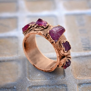Pode incluir: Um anel de cobre com uma banda texturizada e quatro pedras preciosas cor-de-rosa engastadas na banda.