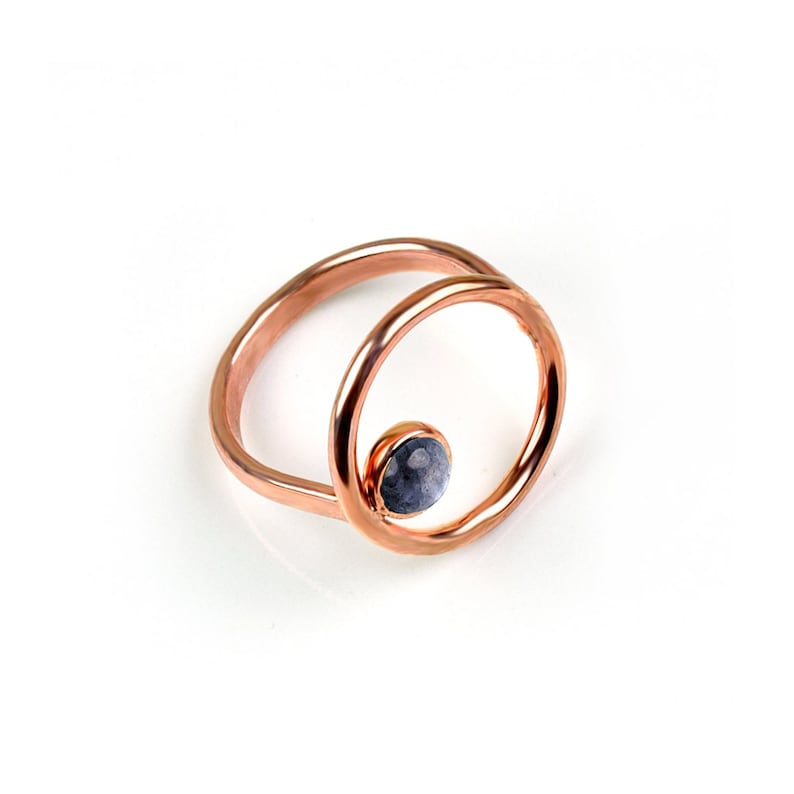 Puede incluir: Un anillo de oro rosa con una sola piedra preciosa redonda gris engastada en un c&iacute;rculo dentro de un c&iacute;rculo m&aacute;s grande.