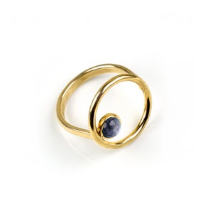 Puede incluir: Anillo de oro con una piedra preciosa azul engastada en un dise&ntilde;o circular.