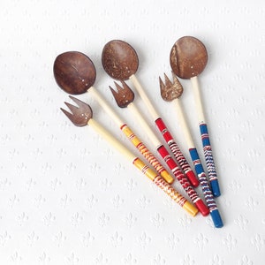 May include: Set of five wooden spoons with forks, made from coconut shells. The spoons are painted with red, yellow, and blue stripes.