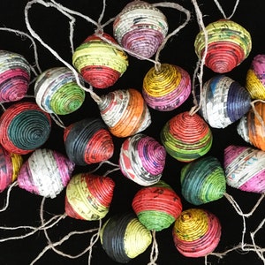 Könnte beinhalten: Eine Sammlung bunter, handgefertigter Ornamente aus gerollten Papier. Die Ornamente sind mit verschiedenen Mustern und Farben verziert, darunter Rot, Grün, Gelb, Blau und Pink. Sie sind mit Schnur aneinandergereiht und wären eine einzigartige und festliche Ergänzung für jede Weihnachtsdekoration.