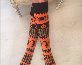 Op de afbeelding: Een paar oranje en zwarte gebreide kniekousen met een Halloween-thema. De sokken hebben pompoenen, vleermuizen en sterren.