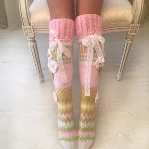 May include: A pair of pink and green knitted knee-high socks with white lace and flower embellishments.